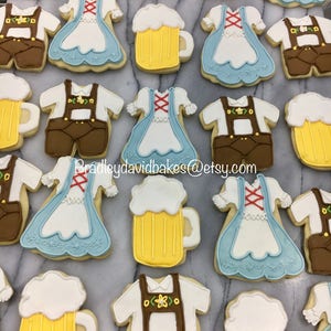 May include: A collection of decorated sugar cookies featuring various designs, including beer steins, lederhosen, and dirndl dresses. The cookies are decorated with white, yellow, brown, and blue icing.