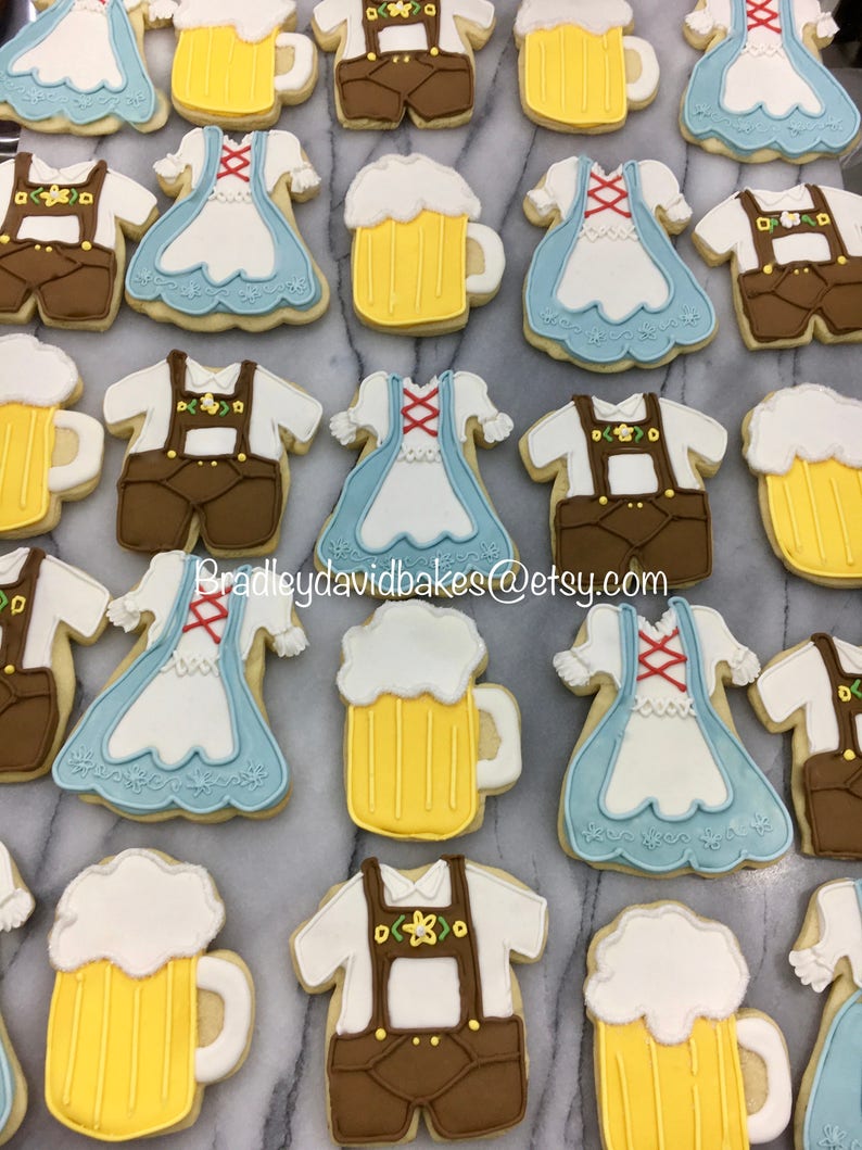 May include: A collection of decorated sugar cookies featuring various designs, including beer steins, lederhosen, and dirndl dresses. The cookies are decorated with white, yellow, brown, and blue icing.