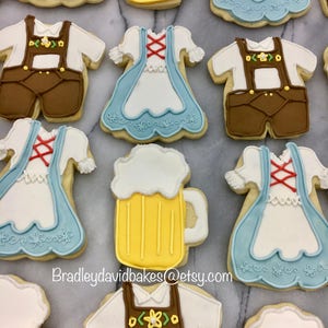 May include: A collection of decorated sugar cookies featuring a variety of designs, including beer steins, dirndls, and lederhosen. The cookies are decorated with white, blue, brown, and yellow icing. The text "Bradleydavidbakes@etsy.com" is visible in the image.