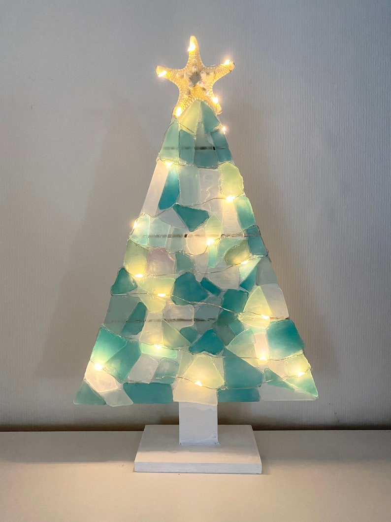 May include: A teal and white sea glass Christmas tree with a starfish on top and white lights. The tree is on a white base.