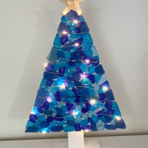 May include: A blue and white sea glass Christmas tree with white lights and a starfish on top. The tree is on a white wooden base.