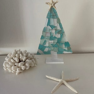 May include: A teal blue and white mosaic Christmas tree with a white starfish on top. The tree is on a white stand and there are two white starfish on a white surface.