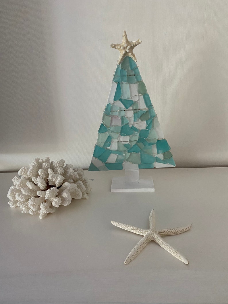 May include: A teal blue and white mosaic Christmas tree with a white starfish on top. The tree is on a white stand and there are two white starfish on a white surface.