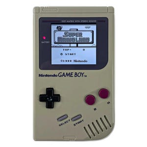 May include: A beige Nintendo Game Boy handheld gaming console with a black and white screen displaying the game Super Mario Land. The console has a red power button, a black directional pad, and two red buttons labeled A and B.
