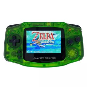 May include: A green Game Boy Advance handheld gaming console with a clear green shell. The screen displays the game "The Minish Cap" from the Zelda series. The text "GAME BOY ADVANCE" is printed on the front of the console.