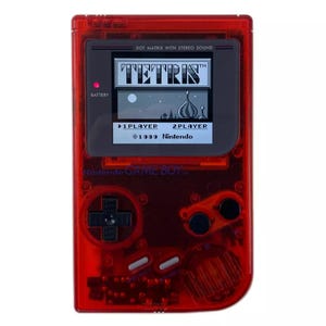 May include: A red transparent Game Boy Color handheld gaming console with a black and white screen displaying the game Tetris. The screen also shows the text "DOT MATRIX WITH STEREO SOUND", "TETRIS", "1 PLAYER", "2 PLAYER", "1939 Nintendo", and "Nintendo GAME BOY".