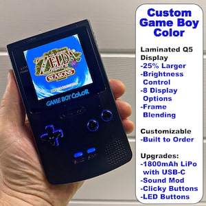 May include: A black Game Boy Color handheld gaming console with a larger, laminated Q5 display. The console is playing The Legend of Zelda: Oracle of Seasons. The console has customizable features, including brightness control, display options, frame blending, and upgrades like a 1800mAh LiPo battery with USB-C charging, a sound mod, clicky buttons, and LED buttons.