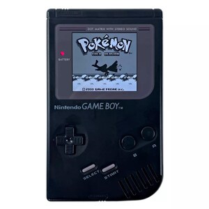 May include: A black Game Boy Color handheld video game console with a gray screen displaying the Pokemon video game. The screen shows a black and white image of a bird-like Pokemon flying in the air. The text "Pokemon" is displayed on the screen in white letters. The text "DOT MATRIX WITH STEREO SOUND" is displayed on the console in white letters. The text "Nintendo GAME BOY" is displayed on the console in white letters. The console has a black D-pad, two black buttons labeled "A" and "B", and two black buttons labeled "SELECT" and "START".