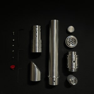 May include: An assortment of disassembled metallic components, including cylindrical tubes, angled pieces, and smaller parts like screws and a red button, arranged on a black surface. The pieces have a brushed metal finish.