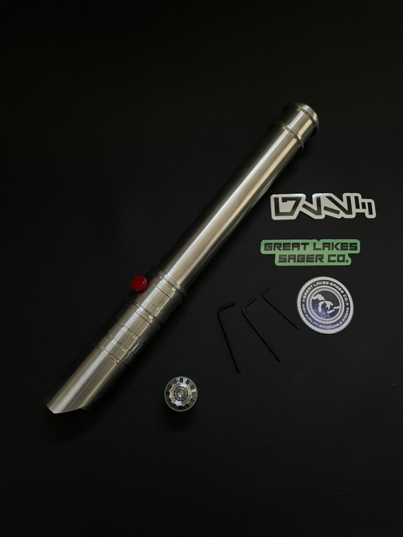 May include: A silver lightsaber with a red button, a silver pommel, and three small black hex keys. The lightsaber is next to stickers that say "DNNH" and "Great Lakes Saber Co."