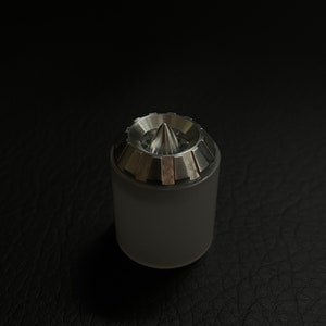 May include: A cylindrical, frosted glass object with a metallic, conical top. The top has a series of rectangular, silver-colored segments around the base of the cone. The object is set against a dark, textured background.