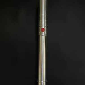 May include: A silver-colored lightsaber with a red button. The hilt has a cylindrical design with ridged sections and a smooth, polished finish. The lightsaber is a prop or toy, likely for cosplay or display.