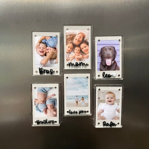 Puede incluir: Seis marcos de fotos de acrílico transparente con bordes blancos, cada uno con una fotografía diferente. Los marcos están fijados a una superficie metálica. Cada marco tiene una palabra o frase en cursiva negra: "bros", "mom", "Leo", "Brothers", "love you" y "Papa".