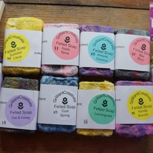 May include: An assortment of felted soaps in different colours, each labelled with its scent, including lavender, citrus, and almond coconut. A wooden soap dish and a tag with the number 024 are also present.