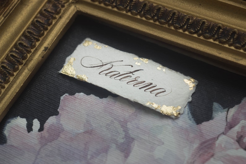 K&ouml;nnte beinhalten: Eine wei&szlig;e Papierkarte mit Blattgoldakzenten und dem Wort "Aterna" in Kalligraphie geschrieben.