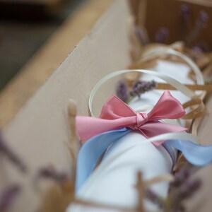 Puede incluir: Un paquete blanco envuelto en papel marr&oacute;n y atado con una cinta rosa y azul. El paquete est&aacute; decorado con flores de lavanda secas.