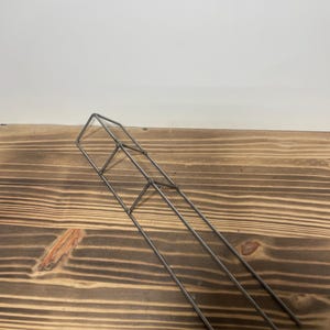 May include: A silver metal plant support with three vertical bars and a square top. The support is made of thin metal and is designed to help plants grow upright.
