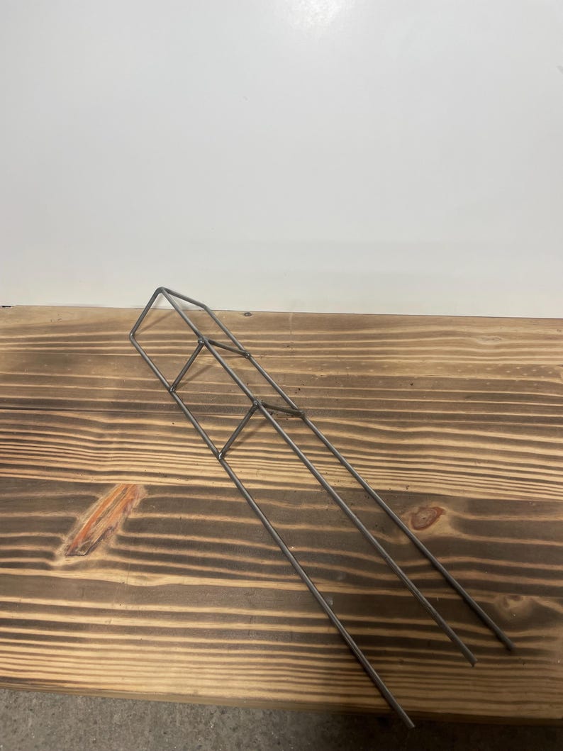 May include: A silver metal plant support with three vertical bars and a square top. The support is made of thin metal and is designed to help plants grow upright.