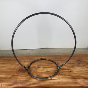 May include: A metal hoop stand with a circular base. The stand is made from a single piece of metal and is designed to hold a variety of items.