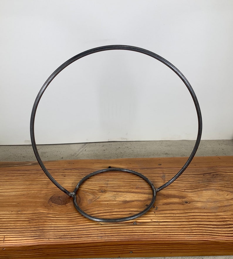 May include: A metal hoop stand with a circular base. The stand is made from a single piece of metal and is designed to hold a variety of items.