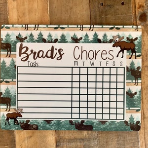 K&ouml;nnte beinhalten: Ein wei&szlig;er Trockenl&ouml;sch-Chore-Chart mit einem Elch- und Waldmotiv. Der Chart hat Platz f&uuml;r einen Namen, "Brad's Chores", und einen Bereich f&uuml;r Aufgaben mit den Wochentagen, die oben aufgelistet sind.