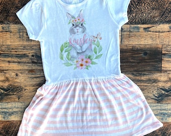 May include: White dress with pink and white stripes. The top of the dress features a watercolour illustration of a bunny wearing a flower crown with the name "Kinsley" written below it.