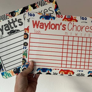 K&ouml;nnte beinhalten: Zwei wei&szlig;e Trockenl&ouml;sch-Chore-Charts mit einem Rennwagen-Thema. Die obere Karte sagt "Wyatt's Chores" und die untere Karte sagt "Waylon's Chores". Beide Karten haben einen Platz f&uuml;r eine Aufgabe und ein Raster f&uuml;r jeden Tag der Woche.