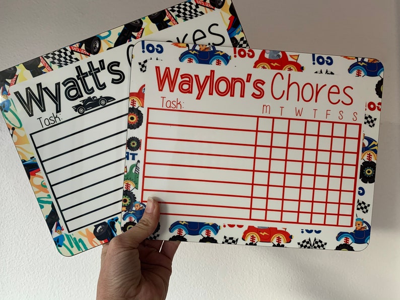 K&ouml;nnte beinhalten: Zwei wei&szlig;e Trockenl&ouml;sch-Chore-Charts mit einem Rennwagen-Thema. Die obere Karte sagt "Wyatt's Chores" und die untere Karte sagt "Waylon's Chores". Beide Karten haben einen Platz f&uuml;r eine Aufgabe und ein Raster f&uuml;r jeden Tag der Woche.