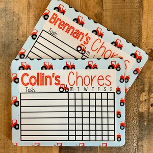 K&ouml;nnte beinhalten: Zwei blaue und wei&szlig;e Aufgabenkarten mit roten Traktor-Illustrationen. Die obere Karte lautet "Brennan's Chores" und die untere Karte lautet "Collin's Chores". Beide Karten haben einen Platz f&uuml;r eine Aufgabe und ein Raster f&uuml;r jeden Tag der Woche.