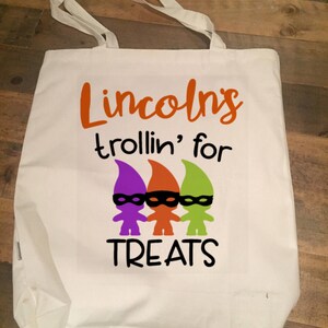 May include: White canvas tote bag with the text "Lincolns trollin' for treats" in orange, purple, and green. Three gnomes with black eye masks are pictured below the text.