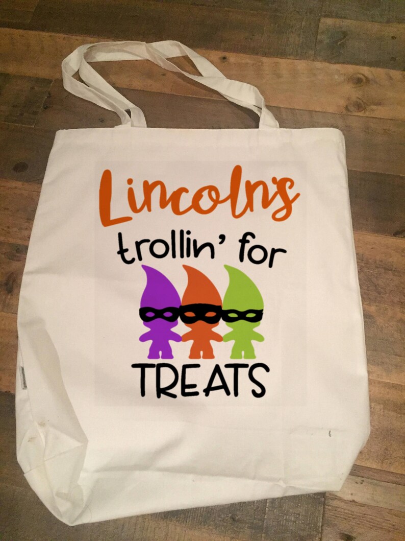 May include: White canvas tote bag with the text "Lincolns trollin' for treats" in orange, purple, and green. Three gnomes with black eye masks are pictured below the text.