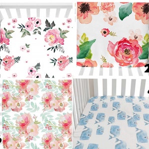 May include: Four crib sheets with different patterns. One sheet features pink floral watercolor designs on a white background. Another has large coral and pink flowers with green leaves. A third sheet has a repeating pattern of pink flowers and green leaves. The last sheet has blue whales.