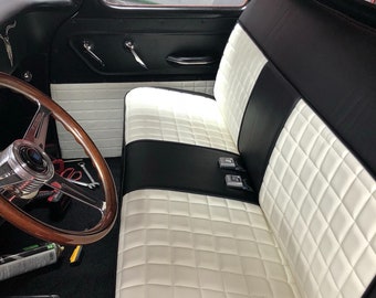 May include: Interior of a classic black truck with a custom white and black diamond-stitched bench seat. The wooden steering wheel and black door panel are visible. The interior has a vintage aesthetic.
