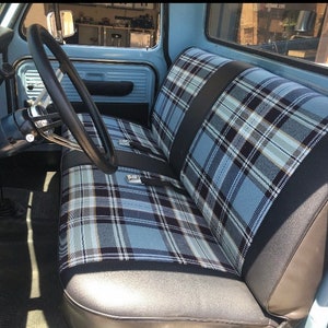 May include: Interior of a light blue classic pickup truck. The seats feature a blue, black, and white plaid design. The steering wheel is black, and the dashboard and door panels are light blue.
