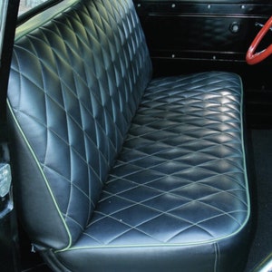 May include: Black bench seat with diamond stitching and light green piping. The seat is in a classic vehicle interior, with a red steering wheel visible in the background. The seat has a vintage aesthetic.