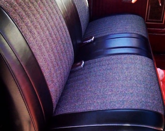May include: A vintage truck bench seat with a two-tone design. The seat features a textured, multi-colored fabric center and black leather-like trim. Seatbelts are visible. The interior is a deep red color.