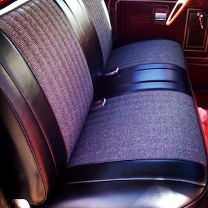 May include: A classic truck bench seat featuring a black leather base and back, with a grey and burgundy patterned fabric centre. The seat has a black leather band and chrome seat belt buckles.