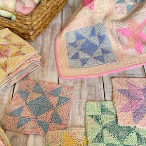 Puede incluir: Una colección de cuadrados tejidos de varios colores, incluyendo rosa, azul, verde y amarillo. Los cuadrados presentan un patrón de estrella y están dispuestos sobre una superficie de madera blanca.