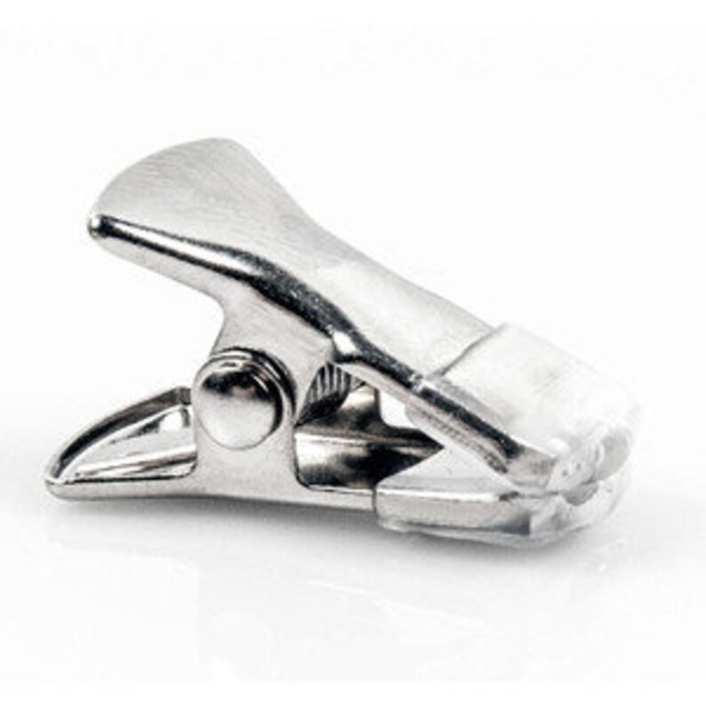 Puede incluir: Una abrazadera de metal plateado con una punta de pl&aacute;stico blanco. La abrazadera se utiliza para sujetar objetos juntos.