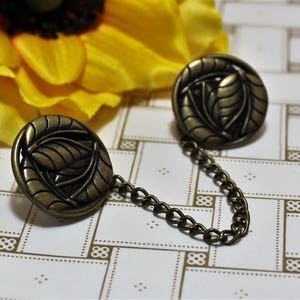 Puede incluir: Un par de broches de metal dorado antiguo con dise&ntilde;o de hojas conectadas por una cadena.