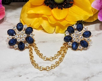 May include: A pair of gold tone brooches with blue and clear rhinestone accents connected by a gold chain.
