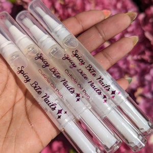May include: Four clear plastic bottles with white caps and a pink label that reads "Spicy Bite Nails Cuticle Oil Pen".