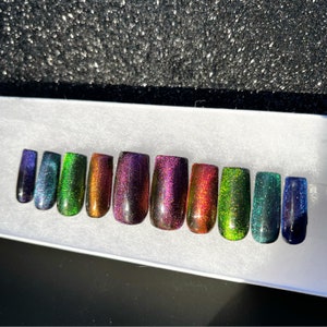 Op de afbeelding: Tien kunstnagels met een holografische glitterafwerking in verschillende kleuren, waaronder groen, paars en blauw.