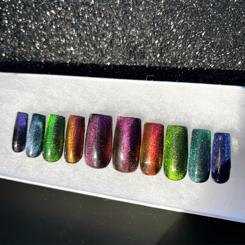 Op de afbeelding: Tien kunstnagels met een holografische glitterafwerking in verschillende kleuren, waaronder groen, paars en blauw.