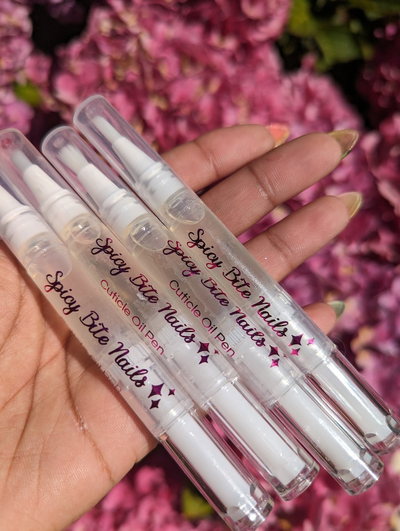 May include: Four clear plastic bottles with white caps and a pink label that reads "Spicy Bite Nails Cuticle Oil Pen".