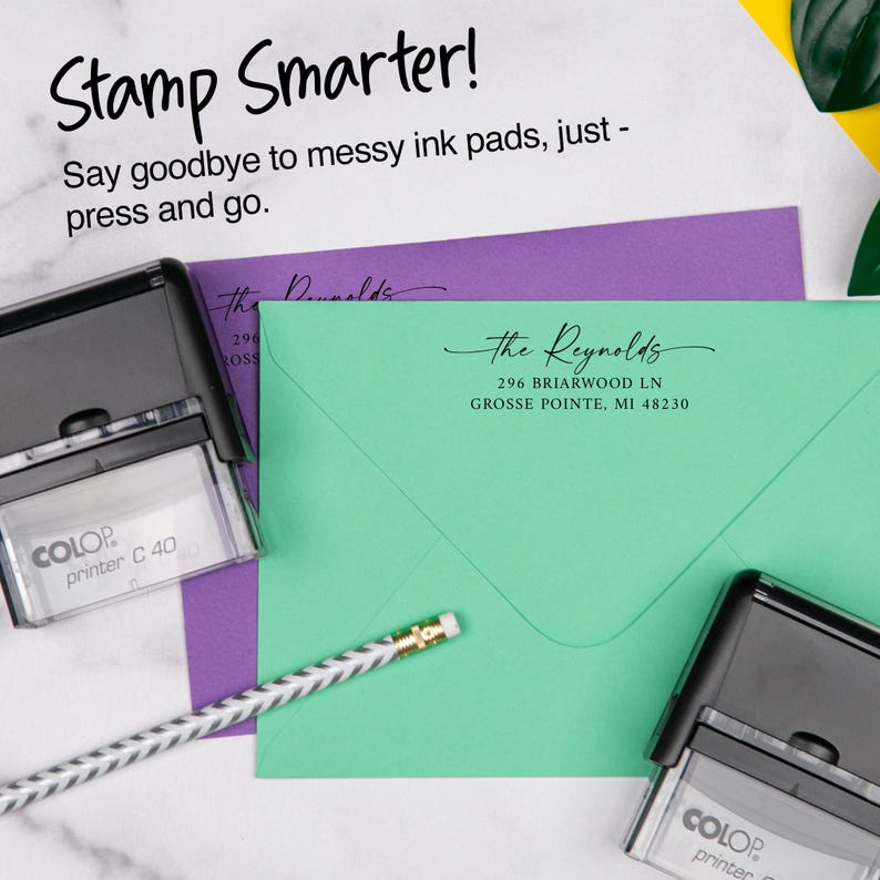 May include: A teal envelope with address details and a black stamp. The text "Stamp Smarter!" and "Say goodbye to messy ink pads, just - press and go" are visible. A pencil and a purple envelope are also in the image.
