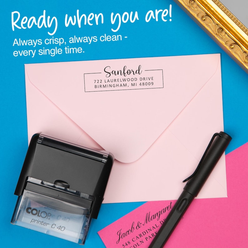 May include: A black and clear self-inking stamp with the text "COLOP printer C 40" next to a pink envelope with the address "Sanford" and a black pen. The background is blue with the text "Ready when you are!"