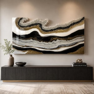 May include: A large rectangular wall art piece featuring abstract, flowing layers of black, white, and gold resin with textured, crystalline accents along the top edge. The composition mimics natural stone formations with a glossy, reflective finish.