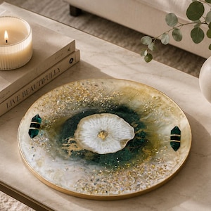 May include: A circular decorative tray with a gold edge, showcasing a central white and gold design encircled by green and gold details. Two dark green and gold decorative accents are on the tray. A lit candle and books are nearby.
