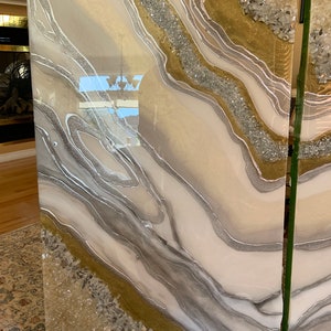 Puede incluir: Dos paneles de arte de resina con un dise&ntilde;o abstracto blanco, dorado y plateado. La resina es transparente y tiene un acabado brillante. El dise&ntilde;o presenta l&iacute;neas en espiral y cristales incrustados.